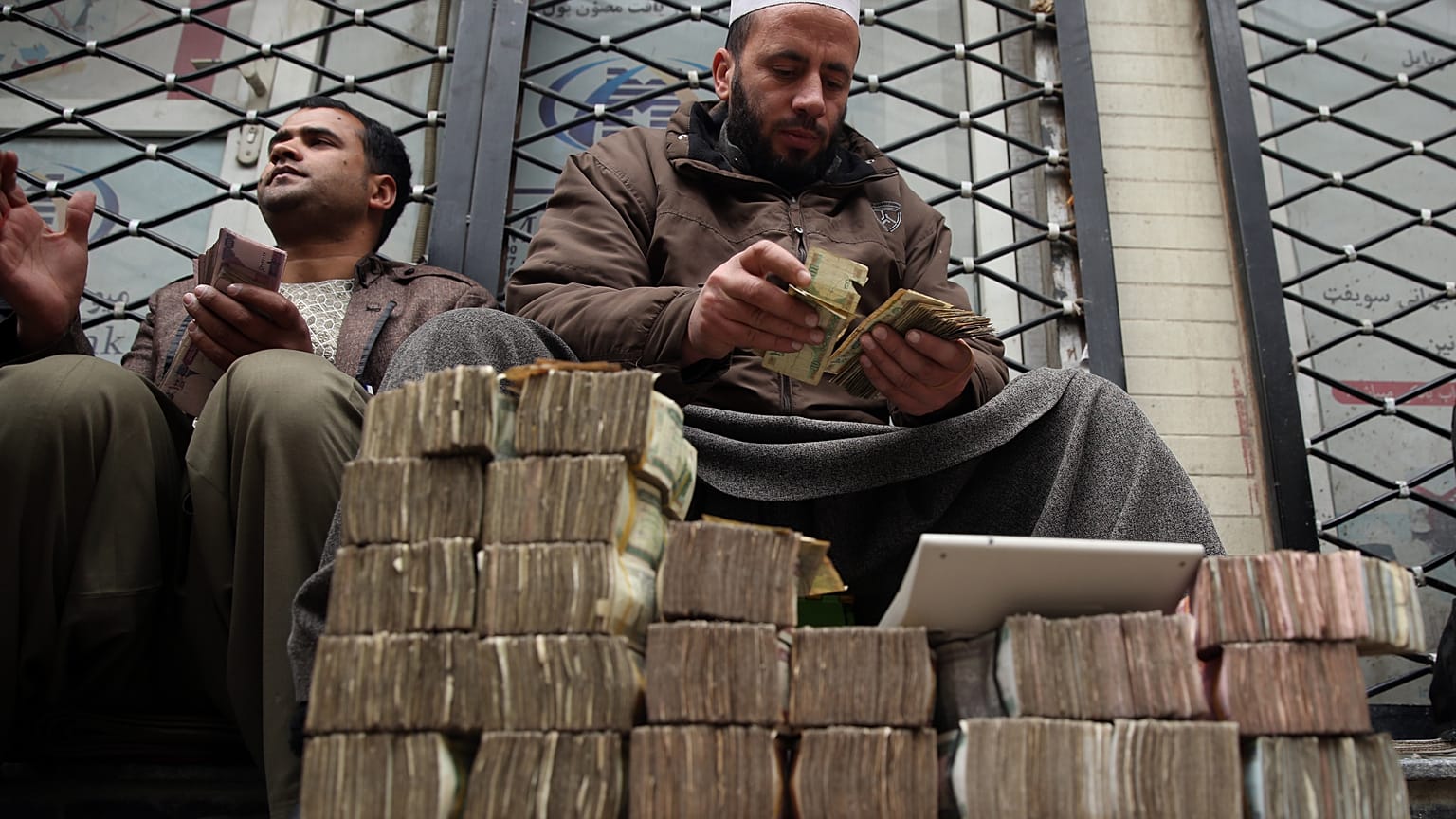 An Afghan money changer, right, counts a pile of currency. Cryptocurrencies, on the other hand, have been a financial lifeline for many Afghans 