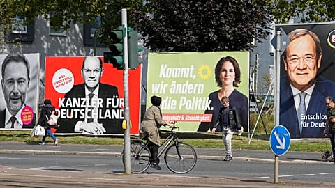 People walk and drive past election posters of the three chancellor candidates in Gelsenkirchen, Germany, Sept. 23, 2021. 