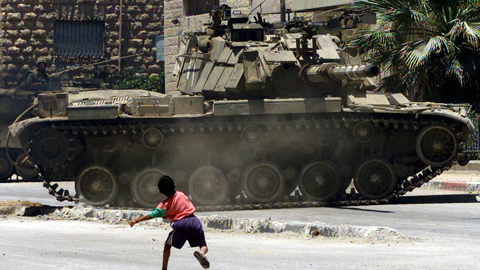طفل فلسطيني يرشق الحجارة باتجاه ناقلة جند إسرائيلية كانت تقوم بدوريات في مخيم الدهيشة للاجئين بالقرب من بيت لحم في 5 يوليو/تموز 2002 أثناء حظر التجول
