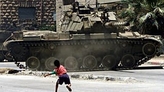 طفل فلسطيني يرشق الحجارة باتجاه ناقلة جند إسرائيلية كانت تقوم بدوريات في مخيم الدهيشة للاجئين بالقرب من بيت لحم في 5 يوليو/تموز 2002 أثناء حظر التجول