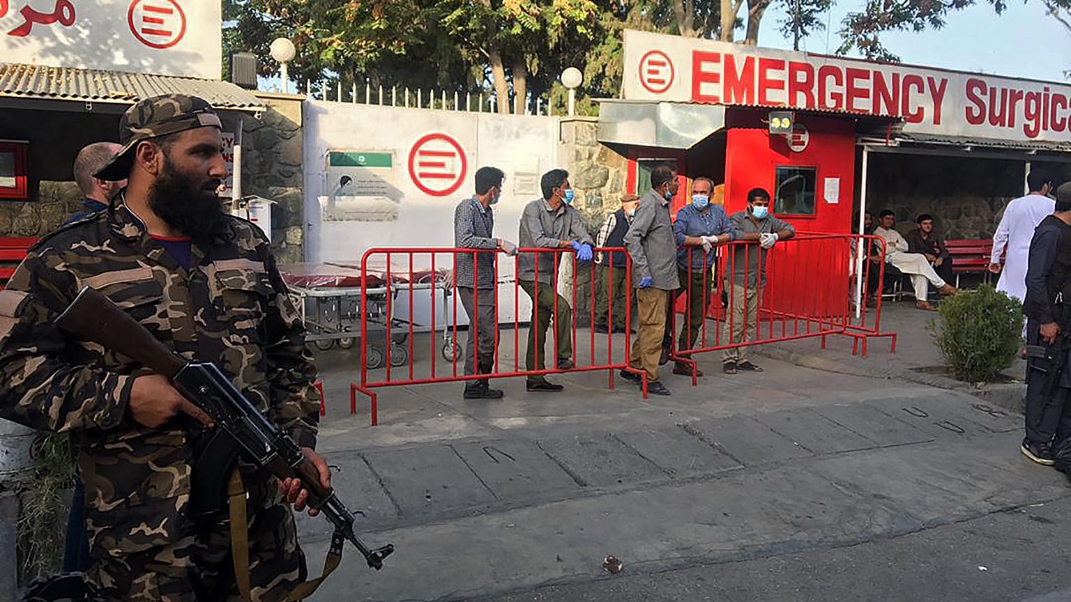 A Taliban fighter (L) stands guard as Afghan medical staff members wait at the entrance of a hospital to receive the victims of an explosion in Kabul on October 3, 2021.
