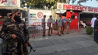 A Taliban fighter (L) stands guard as Afghan medical staff members wait at the entrance of a hospital to receive the victims of an explosion in Kabul on October 3, 2021.