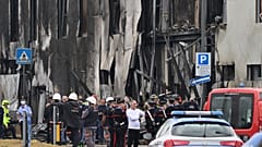 Police and rescue teams stand outside an apparently vacant office building where a small plane crashed in the Milan suburb of San Donato, October 3, 2021.