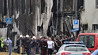 Police and rescue teams stand outside an apparently vacant office building where a small plane crashed in the Milan suburb of San Donato, October 3, 2021.