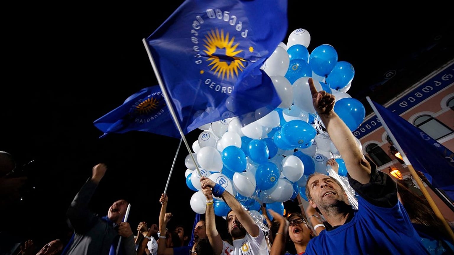 Georgian Dream party supporters cheer, wave flags and hold up balloons.