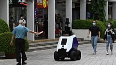 A man gestures to an autonomous robot named "Xavier" as it patrols a shopping and residential district in Singapore.