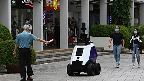 A man gestures to an autonomous robot named "Xavier" as it patrols a shopping and residential district in Singapore.