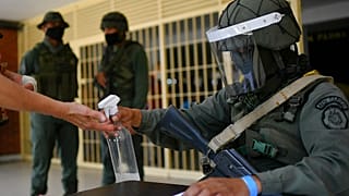 Un soldado echa desinfectante en las manos de un participante en el simulacro electoral en El Valle, Caracas