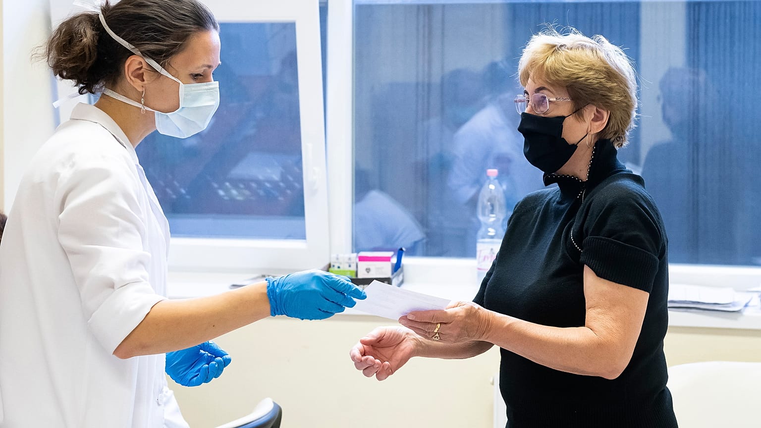 Átadják egy nőnek az oltási igazolását a harmadik oltás felvétele után
