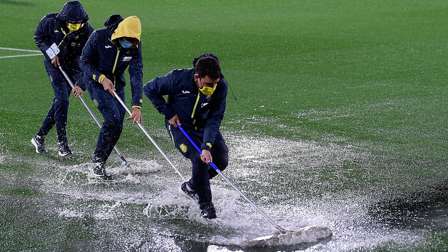 Villareal coaching staff clear water from the pitch following heavy rain before a UEFA Europa League group match