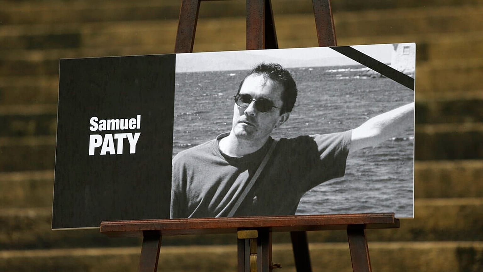 The portrait of slain teacher Samuel Paty with a black ribbon is displayed Tuesday, Oct.20, 2020 on the steps of the National Assembly in Paris. 