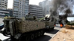 Lebanese army soldiers stand guard protesters burn garbage containers to block a road in Beirut.