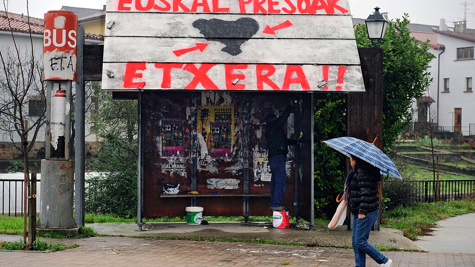 Una mujer pasa por delante de una parada de autobús público en la que se lee en euskera: ''ETA'' a la izquierda, y ''Presos vascos, volved a casa''