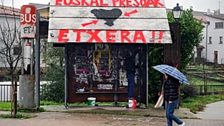 Una mujer pasa por delante de una parada de autobús público en la que se lee en euskera: ''ETA'' a la izquierda, y ''Presos vascos, volved a casa''