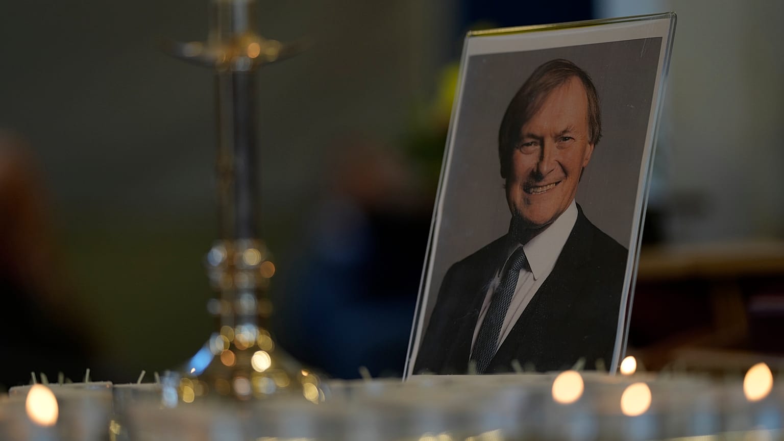 Candles are lit next to a portrait of British Lawmaker David Amess during a vigil for him at St Michaels Church, in Leigh-on-Sea, England Sunday, Oct. 17, 2021.
