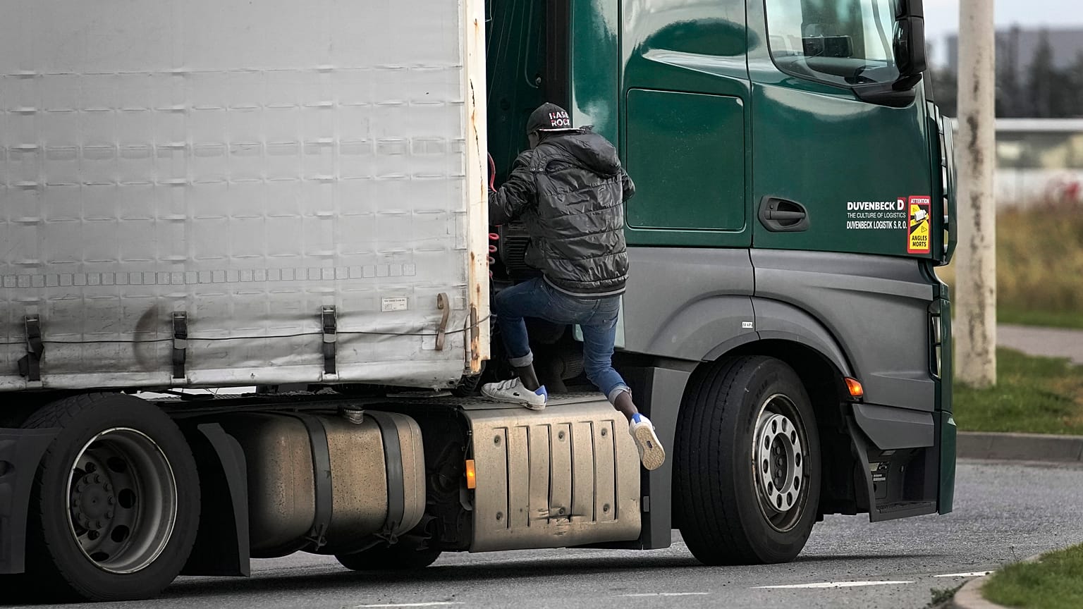 A migrant jumps on a truck in Calais, northern France, Thursday, Oct. 14, 2021, to cross the tunnel heading to Britain. 