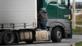 A migrant jumps on a truck in Calais, northern France, Thursday, Oct. 14, 2021, to cross the tunnel heading to Britain. 