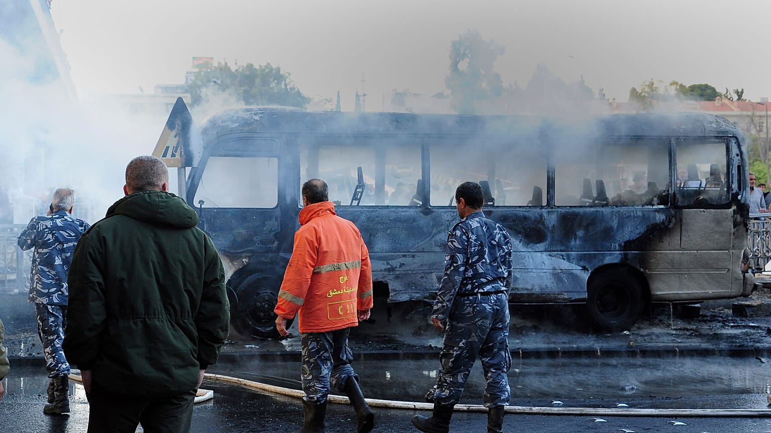 In this photo released by the Syrian official news agency SANA, Syrian firefighters and security officer check a burned bus