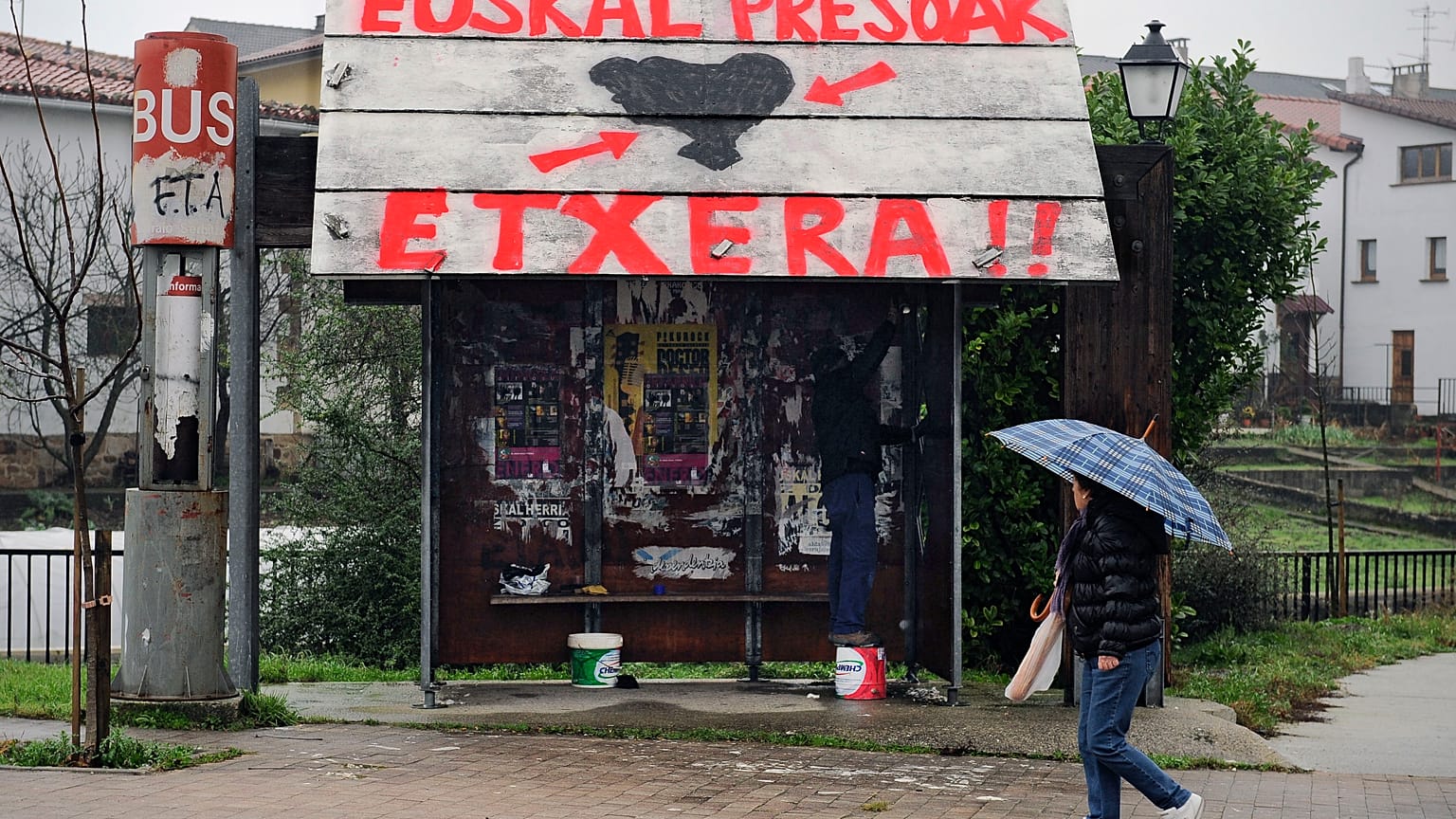 Une femme passe devant un arrêt de bus sur lequel on peut lire en basque "ETA" à gauche et "Prisonniers basques, rentrez chez vous"