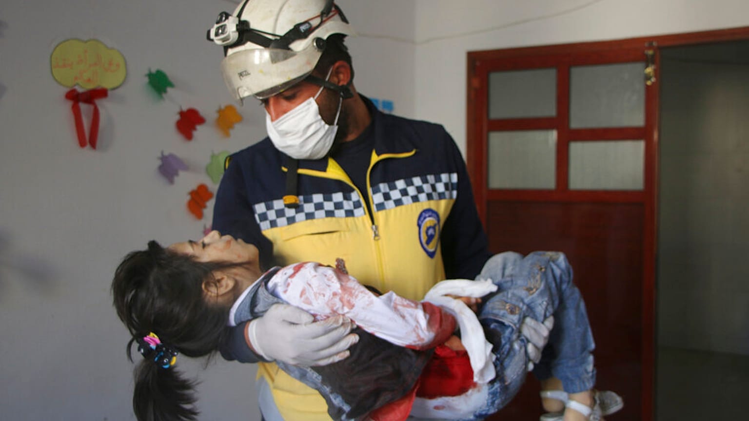 Un casco blanco de la Defensa Civil siria lleva en brazos a una niña herida en el bombardeo