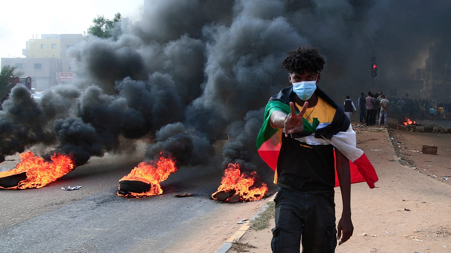 Un manifestante sudanese avvolto nella bandiera nazionale accanto a pneumatici in fiamme durante una manifestazione nella capitale Khartoum, 25 ottobre 2021