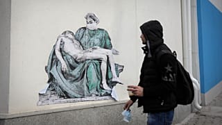 A man passes by replica of Michelangelo's Pieta painted on the wall of Pirogov hospital in Sofia, Sunday, Feb. 7, 2021