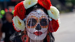Una mujer disfrazada de "Catrina" y con una pantalla facial posa para una foto durante las festividades del Día de Muertos en la Ciudad de México, el 31 de octubre de 2021.