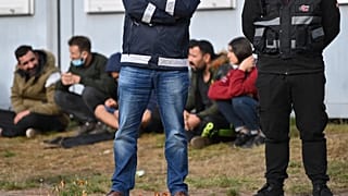 Security guards stand in front of migrants at an asylum facility in Eisenhuettenstadt.
