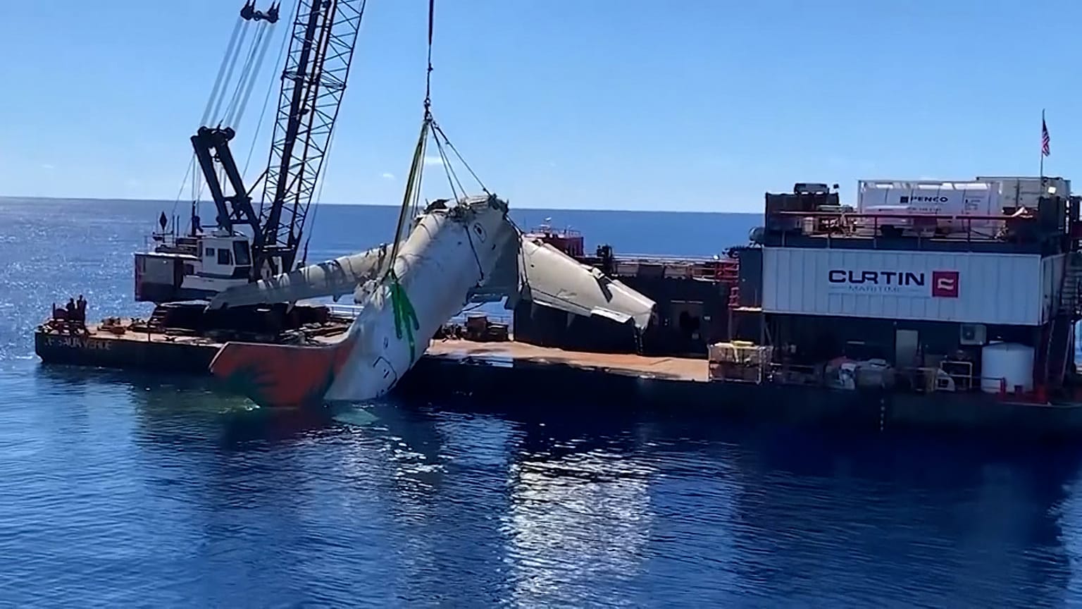 Fuselage of plane being lifted on barge off Honolulu in Hawaii.