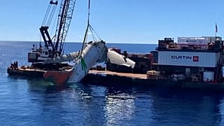 Fuselage of plane being lifted on barge off Honolulu in Hawaii.