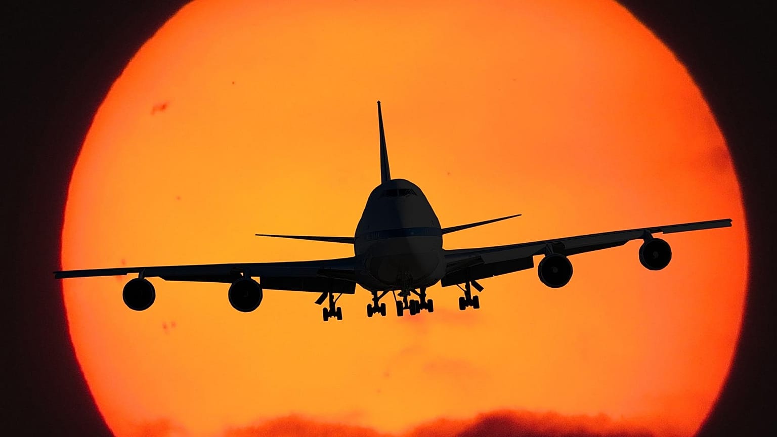 The silhouette of a jet landing with the sun behind it