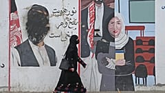 زنی در شهر مزارشریف در حال عبور از کنار یک نقاشی دیواری است