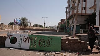 People walk past a barricade in Khartoum, Sudan, Sunday, Nov. 7, 2021.