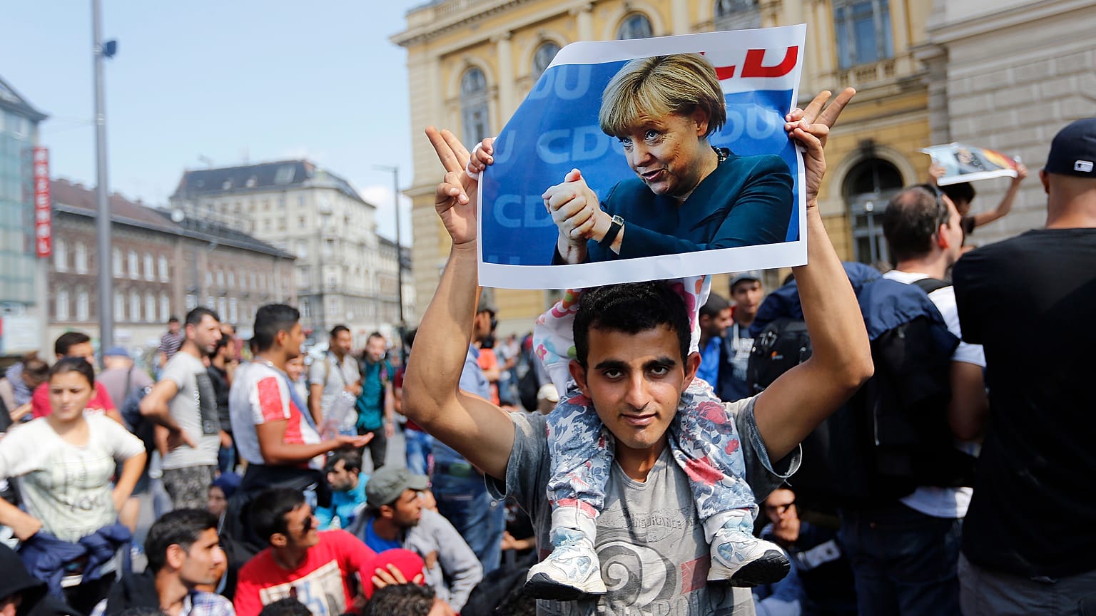 FILE - A migrant holds up a poster of German Chancellor Angela Merkel before starting a march out of Budapest, Hungary, towards Austria and Germany, Sept. 4, 2015