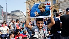FILE - A migrant holds up a poster of German Chancellor Angela Merkel before starting a march out of Budapest, Hungary, towards Austria and Germany, Sept. 4, 2015