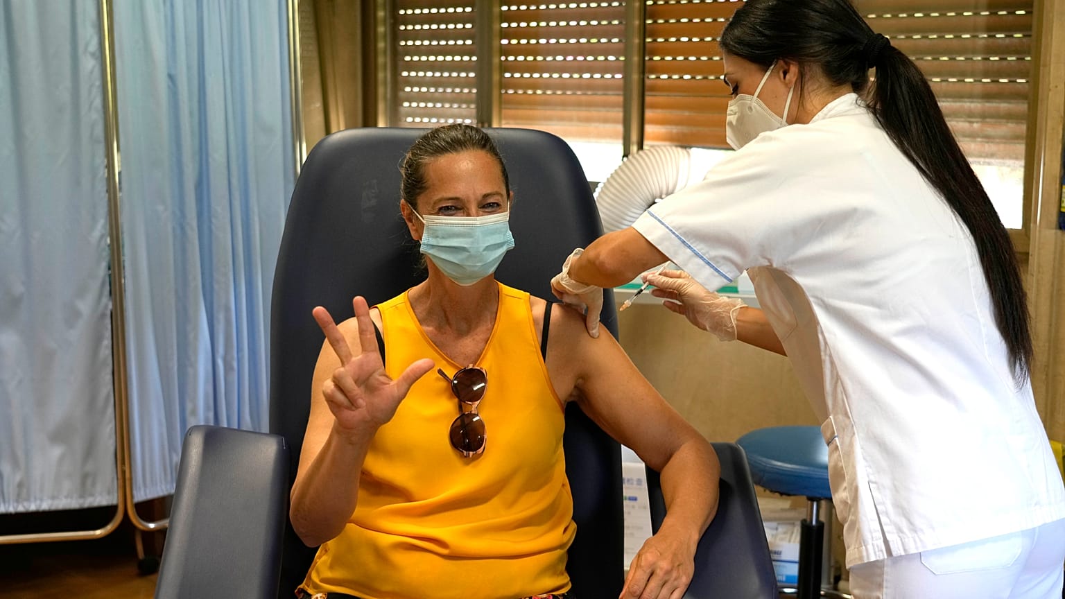 A woman shows the number three as she receives the third shot of Pfizer's Comirnaty vaccine, Sept. 16, 2021, at the Eastman clinic in Rome. 