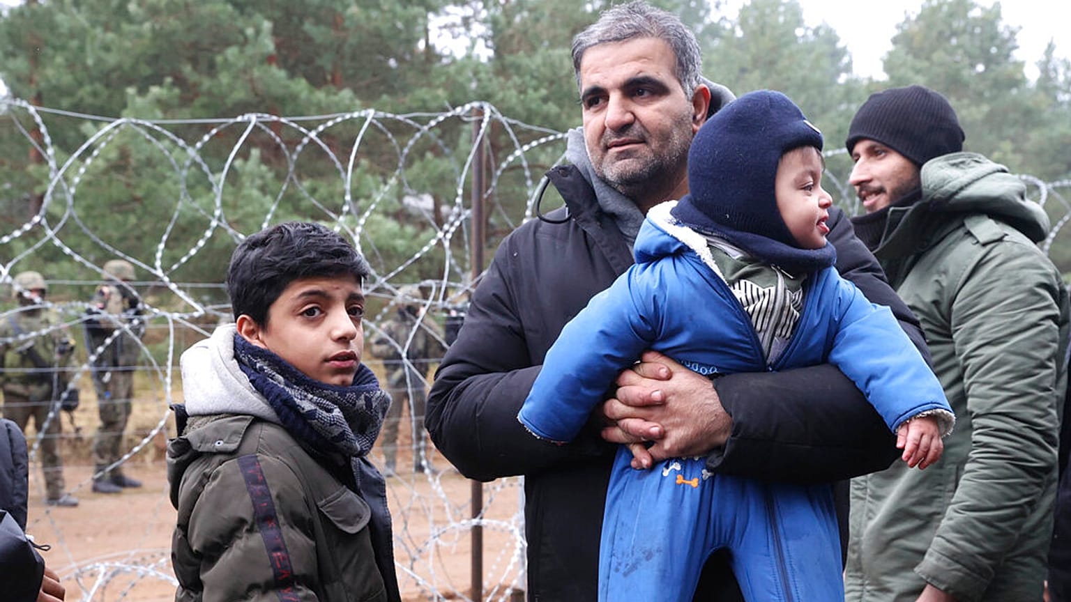 Un homme, un migrant, tenant dans ses bras un bébé, debout aux côtés d'un autre enfant dans le froid, à la frontière entre le Bélarus et la Pologne, 10 novembre 2021
