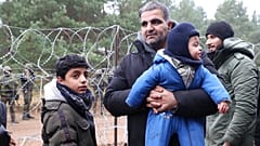 Un homme, un migrant, tenant dans ses bras un bébé, debout aux côtés d'un autre enfant dans le froid, à la frontière entre le Bélarus et la Pologne, 10 novembre 2021