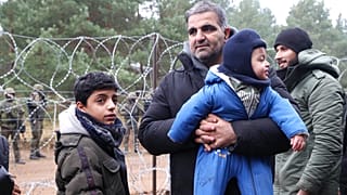 Un homme, un migrant, tenant dans ses bras un bébé, debout aux côtés d'un autre enfant dans le froid, à la frontière entre le Bélarus et la Pologne, 10 novembre 2021