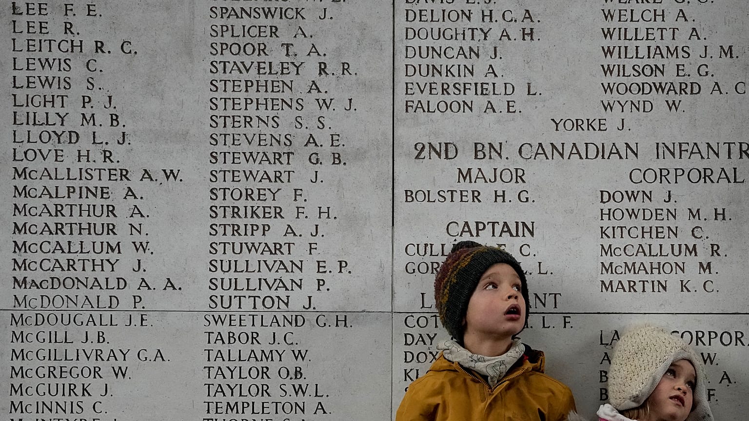 Two children look up at a wall of the missing during an Armistice Day ceremony at the Menin Gate Memorial to the Missing in Ypres, Belgium, Thursday, Nov. 11, 2021. 