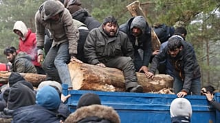 A group of migrants unload a truck with tree trunks delivered by the Belarusian officials in a camp on the Belarusian-Polish border in the Grodno region on November 14, 2021.