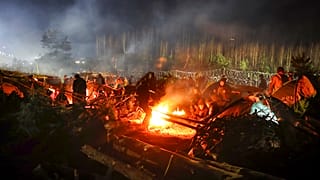 Los migrantes se calientan junto a una hoguera mientras se reúnen en la frontera entre Bielorrusia y Polonia, cerca de Grodno, Bielorrusia, el sábado 13 de noviembre de 2021