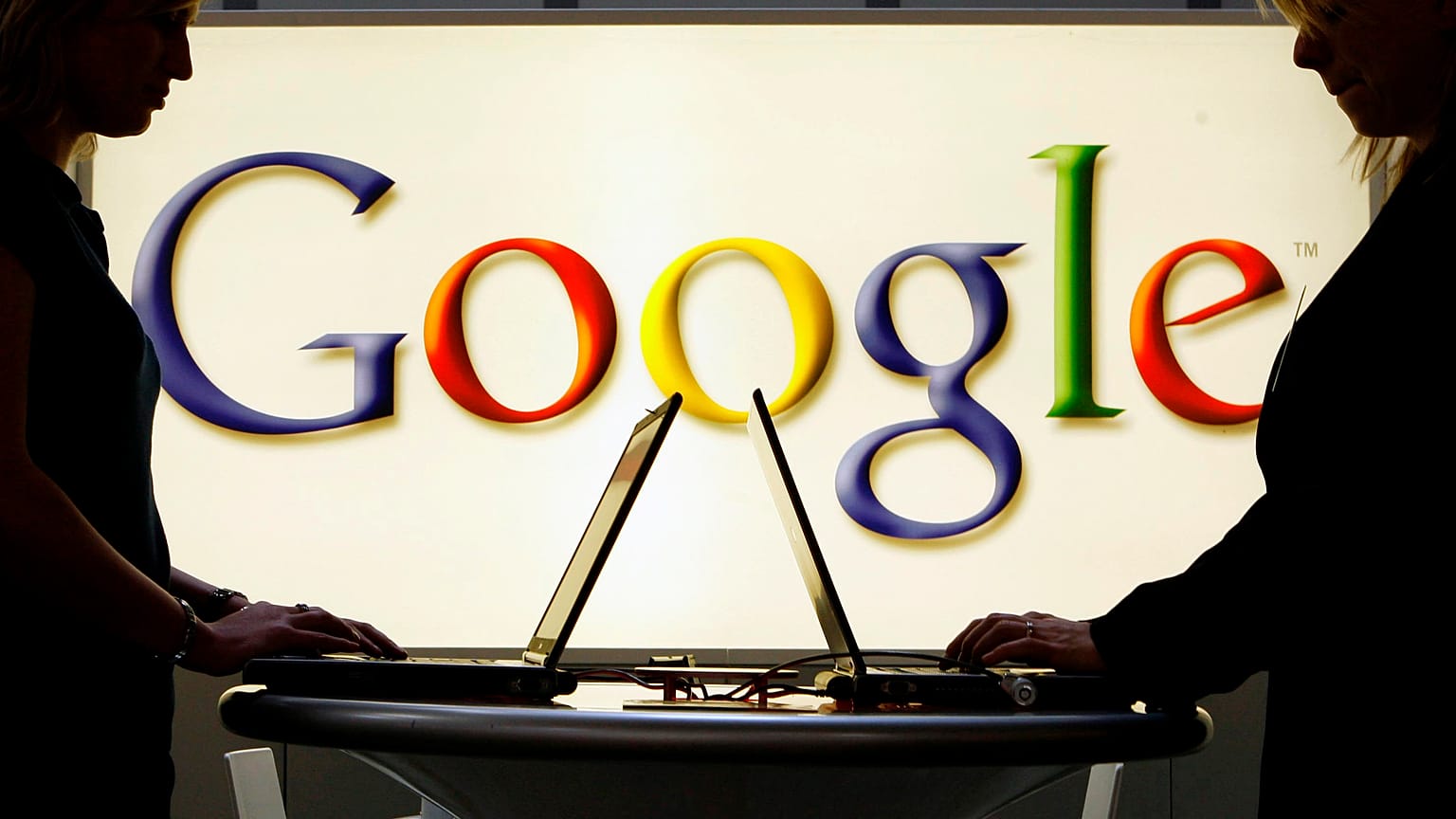 Exhibitors work on laptop computers in front of an illuminated sign of the Google logo at the industrial fair Hannover Messe in Hanover, Germany, April 17, 2007