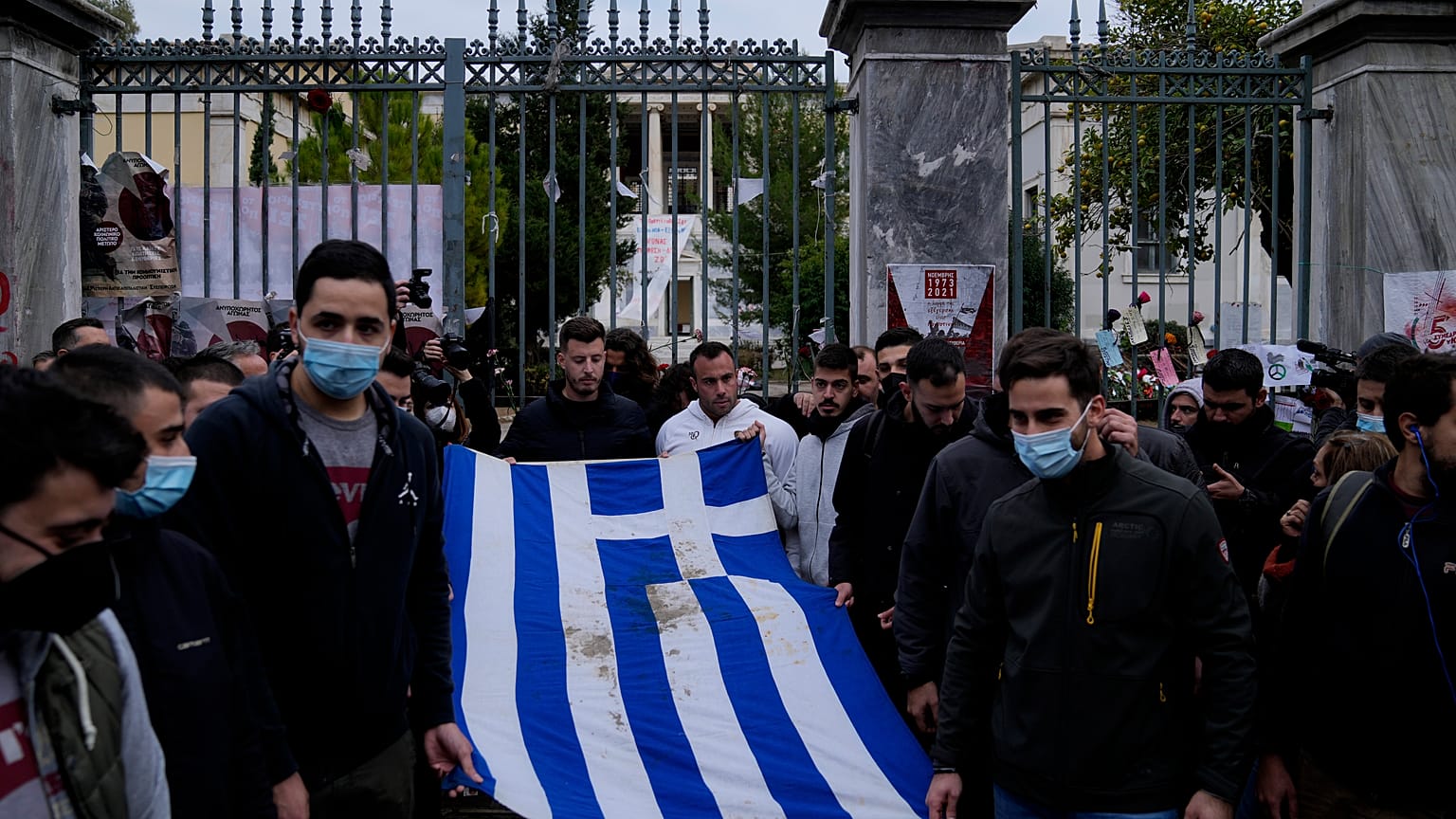 University students stand outside of the Athens Polytechnic and hold a blood-stained Greek flag from the deadly 1973 student uprising during a rally in Athens, Nov. 17, 2021.