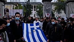University students stand outside of the Athens Polytechnic and hold a blood-stained Greek flag from the deadly 1973 student uprising during a rally in Athens, Nov. 17, 2021.