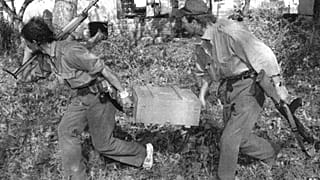 Dos soldados territoriales serbios corren con una caja de granadas capturada en las afueras de la ciudad de Vukovar, Croacia, el viernes 27 de septiembre de 1991