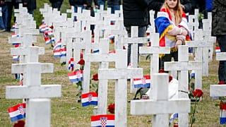 A little girl draped in the Croatian flag looks on at Vukovar's memorial cemerety, in Vukovar, eastern Croatia, Thursday, Nov. 18, 2021. 