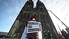 A participant of a rally of the initiative Maria 2.0 holds a poster with the inscription 'No offices for cover-ups' in front of the cathedral in Cologne, Germany.