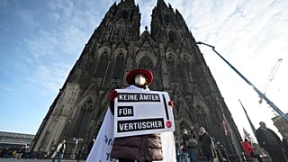 A participant of a rally of the initiative Maria 2.0 holds a poster with the inscription 'No offices for cover-ups' in front of the cathedral in Cologne, Germany.