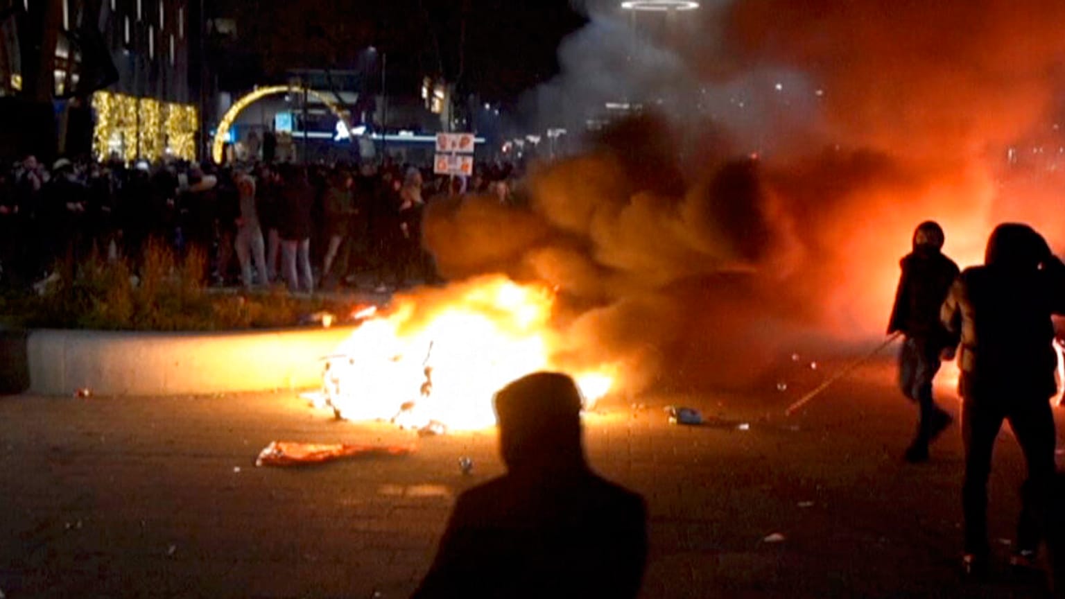 Varios manifestantes encapuchados desafían a las fuerzas del orden tras incendiar un contenedor de basura en Róterdam.